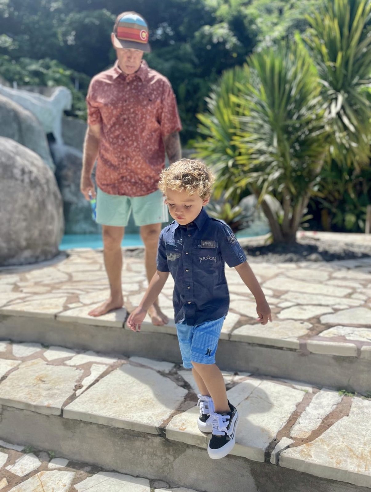 Nikko walking down stone steps toward a pool, looking down at his own feet, with Rob several steps behind him, watching.